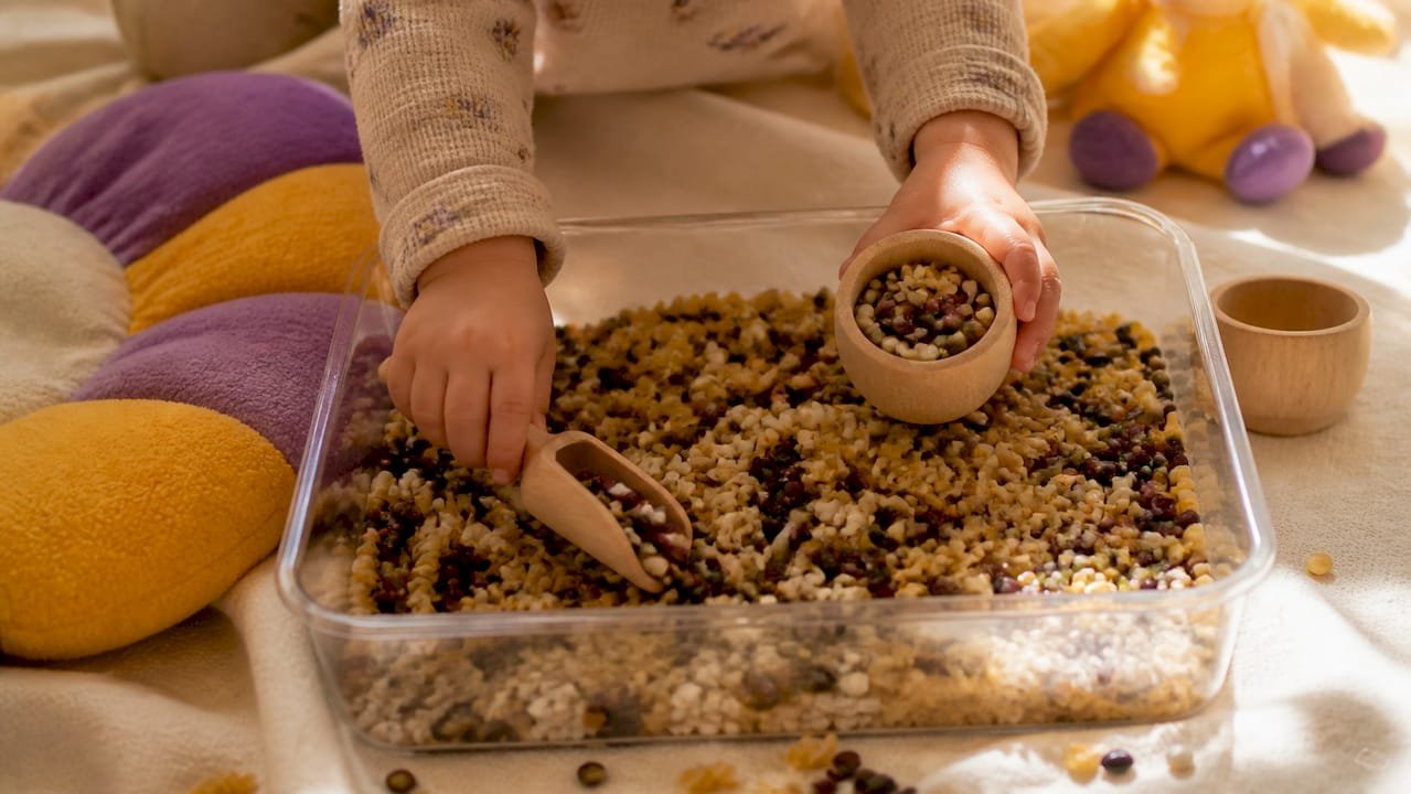 Toddler hands scooping sensory bin on sheet