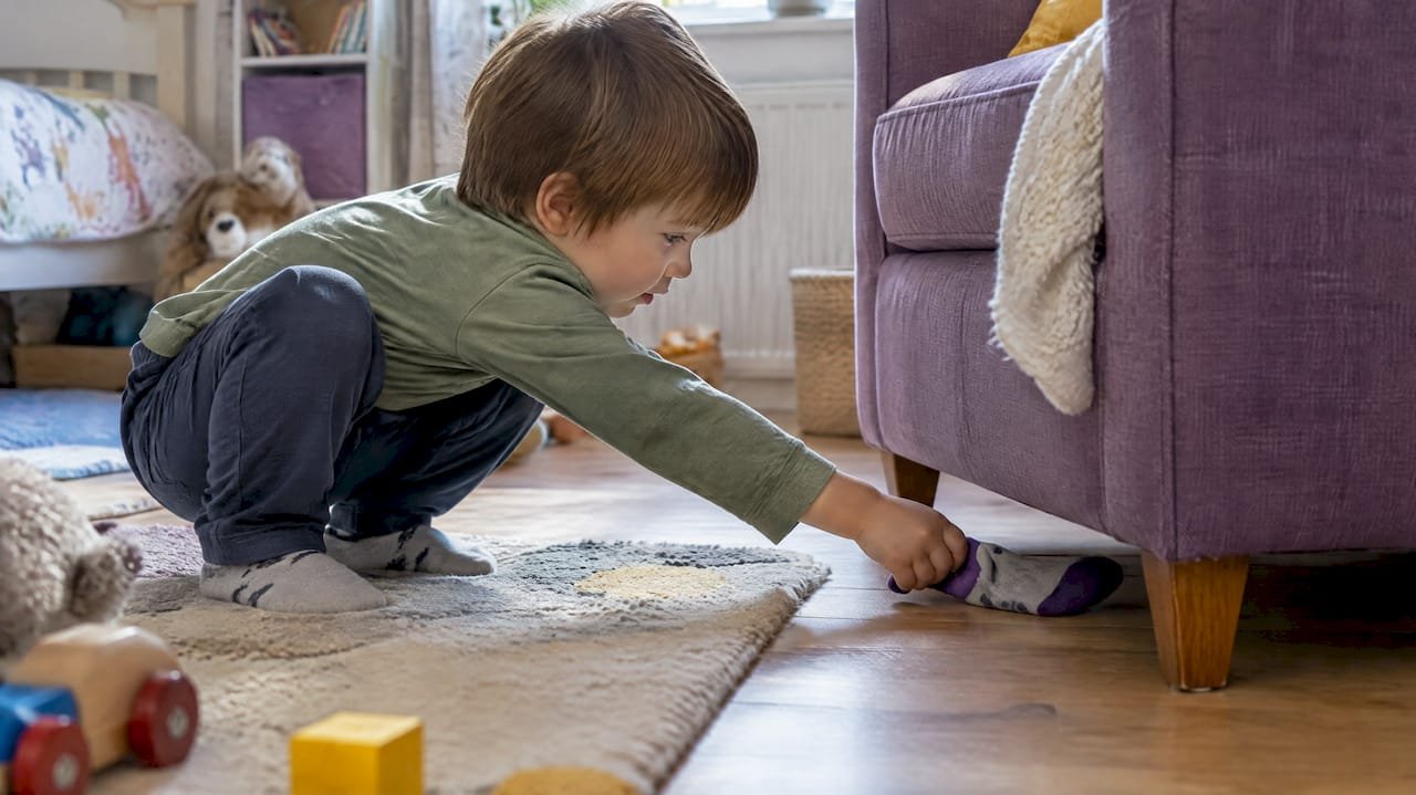 Toddler finding a sock beneath an armchair