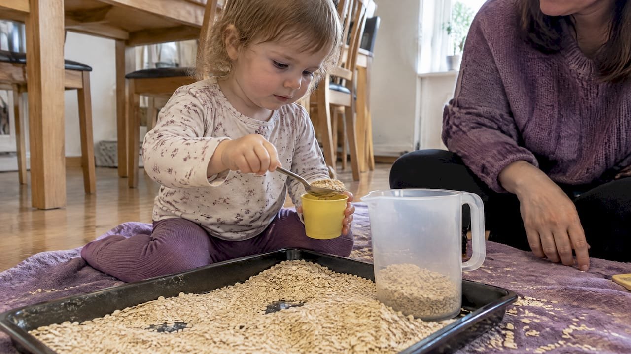 Toddler scooping oats on a tray