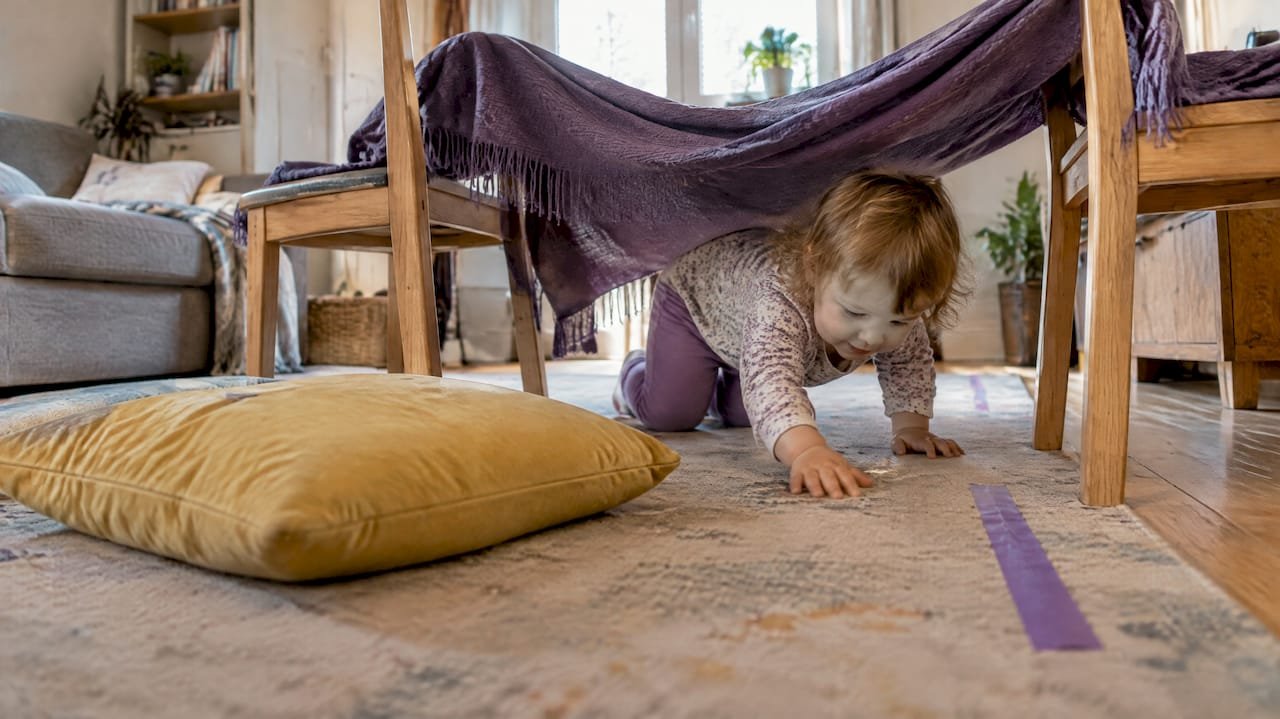 Toddler crawling beneath a blanket tunnel