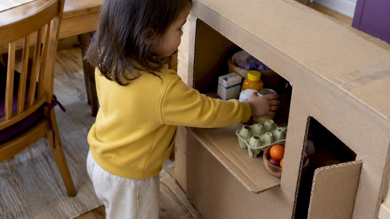 Toddler plays shop at a cardboard box counter