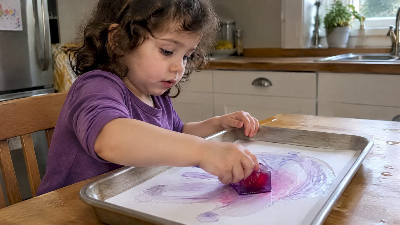 Toddler painting paper with colored ice